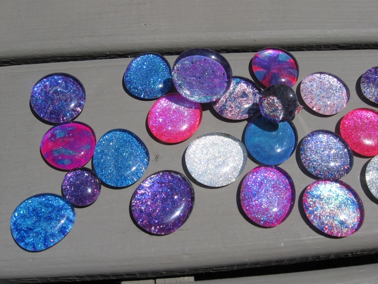 Collection of round glass or resin pieces with sparkly glitter in blue, purple, and pink hues laid on a wooden surface