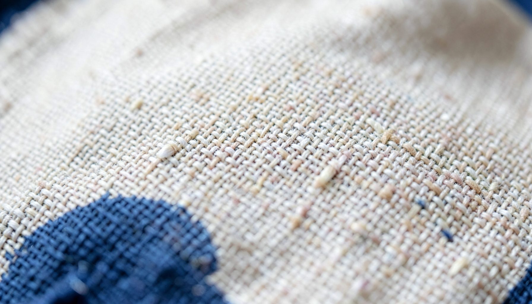 Extreme close-up of woven linen fabric in soft cream and beige tones, showing natural slubs and thread texture under gentle daylight